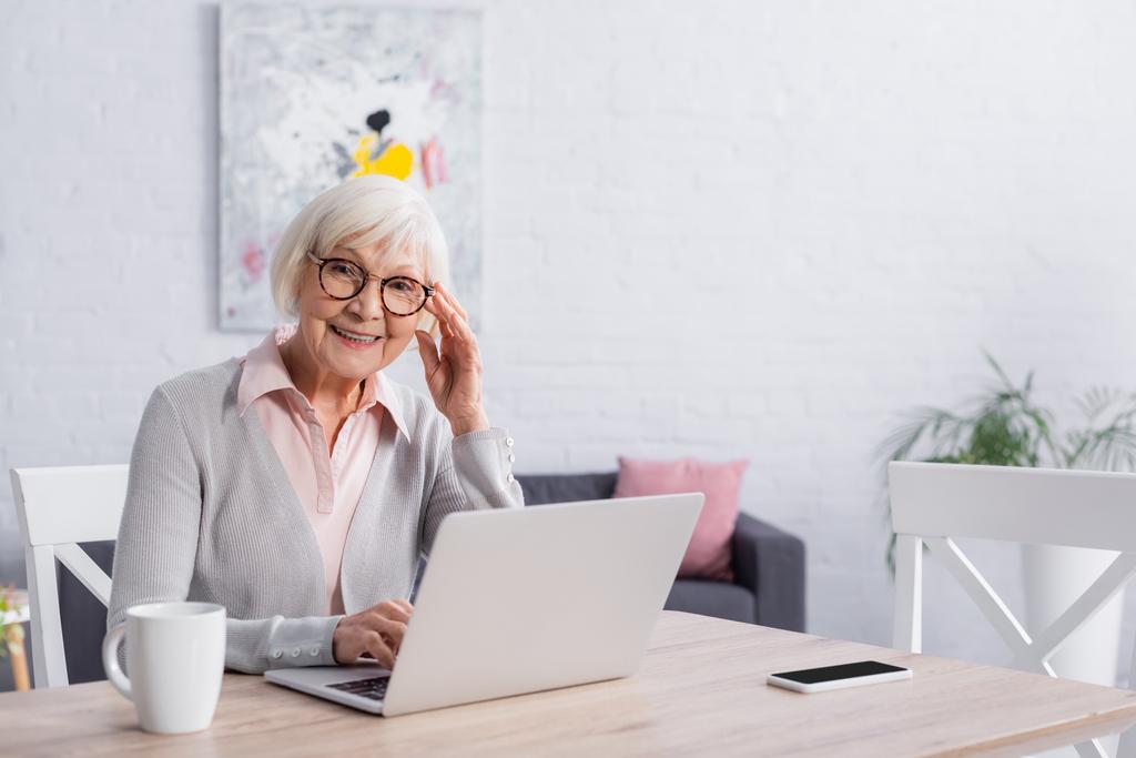 Smiling woman looking at camera near gadgets and cup  - Photo, Image