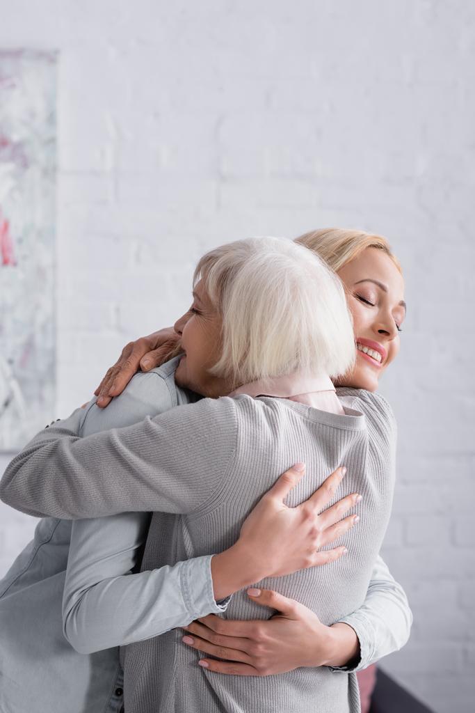 Χαρούμενη γυναίκα που αγκαλιάζει γκριζομάλλη γονέα στο σαλόνι  - Φωτογραφία, εικόνα