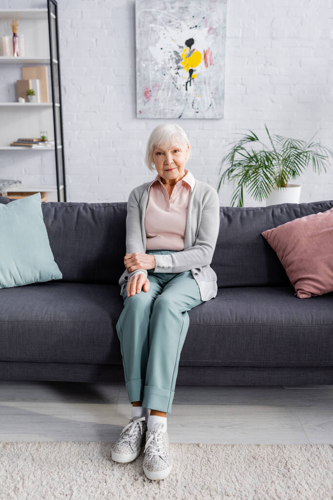 Пожилая женщина смотрит в камеру на диване  - Фото, изображение