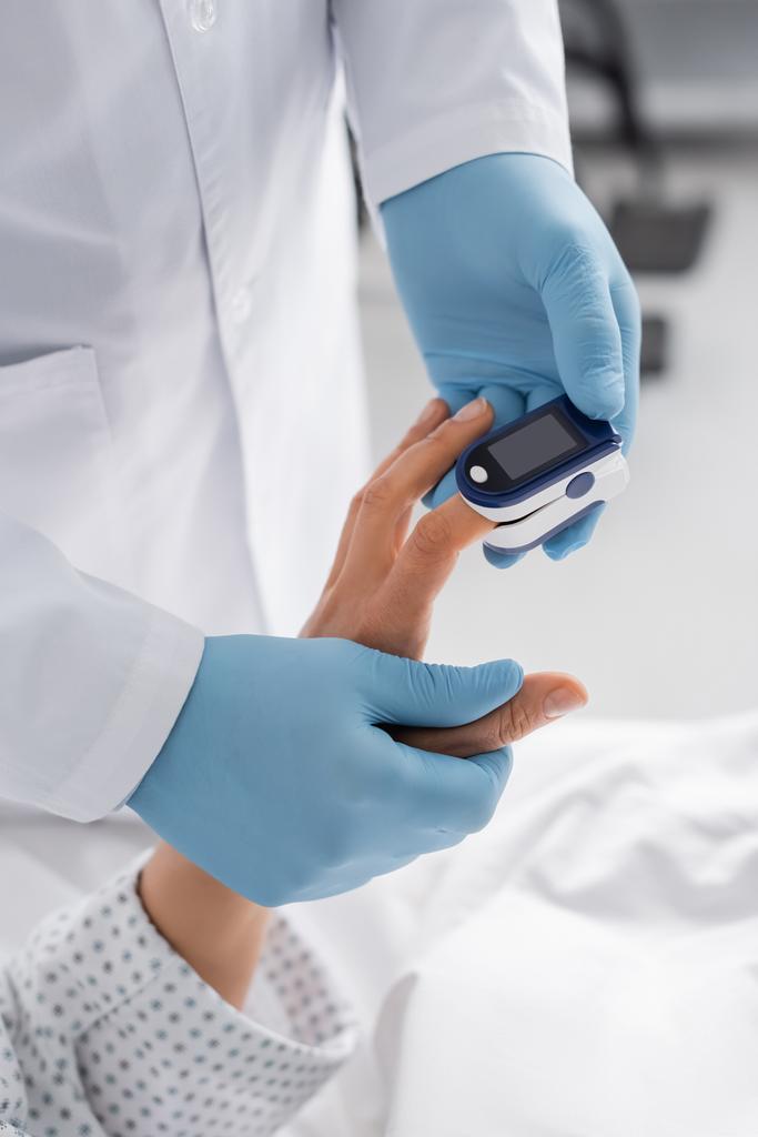 Lateks eldivenli doktorun kırpılmış görüntüsü nabız oksimetresi olan bir kadının kalp atış hızını ölçüyor. - Fotoğraf, Görsel