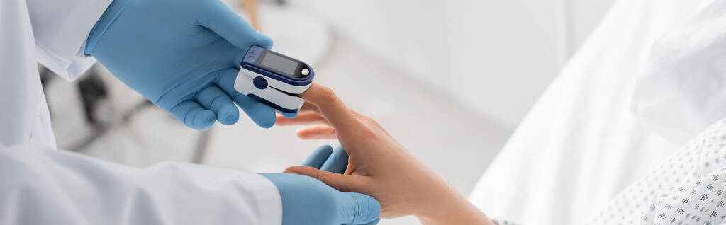 μερική άποψη του γιατρού σε γάντια λατέξ μέτρηση κορεσμού της γυναίκας με παλμικό οξύμετρο, πανό - Φωτογραφία, εικόνα