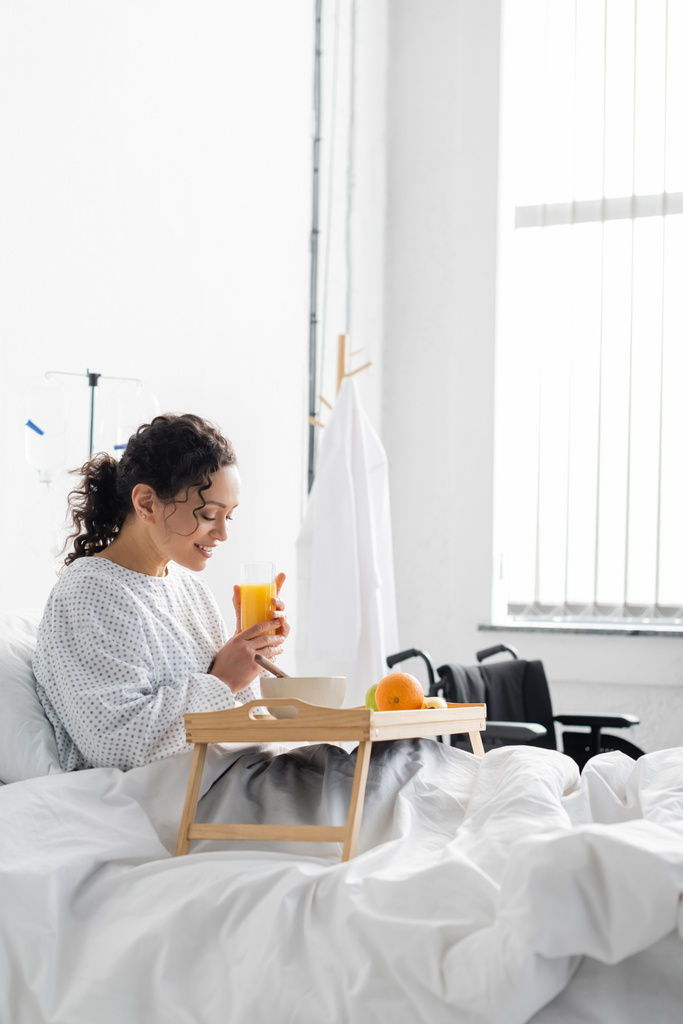 mulher afro-americana positiva tomando café da manhã na cama do hospital - Foto, Imagem