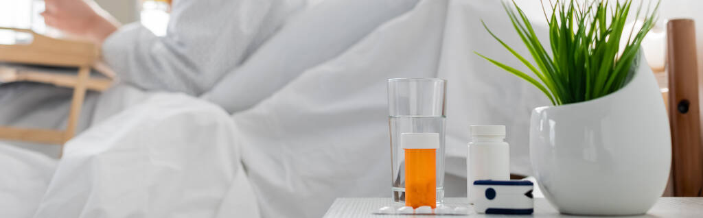 selektivní zaměření léků, pulzní oxymetr, rostlinná a sklenice vody v blízkosti pacienta na rozmazaném pozadí, banner - Fotografie, Obrázek