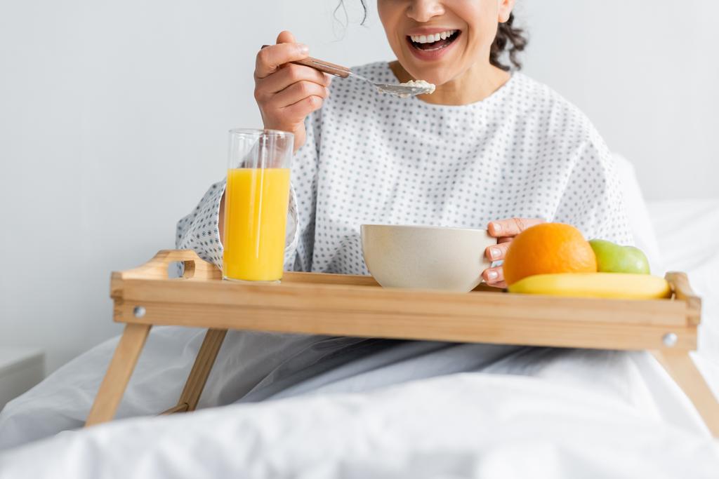 abgeschnittene Ansicht einer lächelnden Afroamerikanerin beim Frühstück im Krankenhaus auf verschwommenem Vordergrund - Foto, Bild