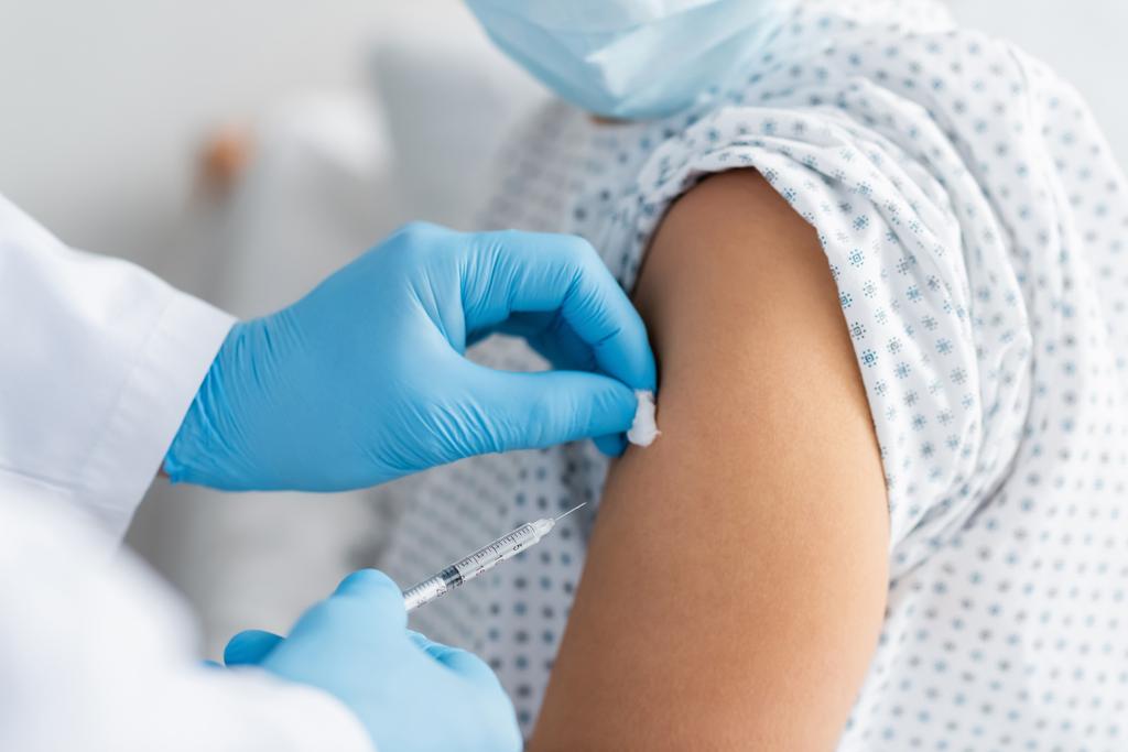 Teilansicht des Arztes in Latexhandschuhen bei der Injektion von Impfstoff an Frau in medizinischer Maske - Foto, Bild