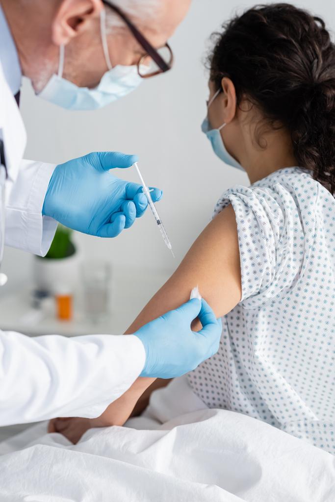 лікар в медичній масці робить ін'єкції вакцини афроамериканській жінці
 - Фото, зображення