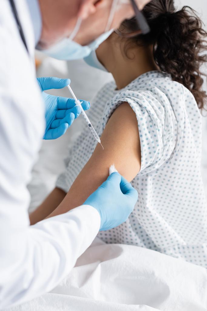 vista ritagliata del medico in guanti di lattice che fa la vaccinazione della donna afro-americana, primo piano sfocato - Foto, immagini