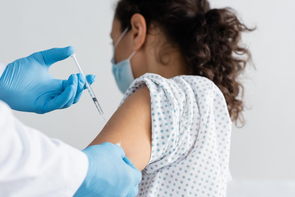 Lateks eldivenli doktor Afrikalı Amerikalı kadına aşı enjekte ediyor. - Fotoğraf, Görsel