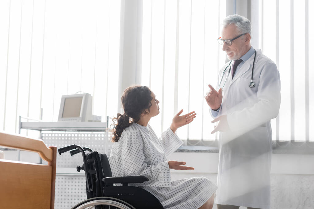 Африканская американка в инвалидном кресле жестикулирует, разговаривая с доктором в больнице - Фото, изображение
