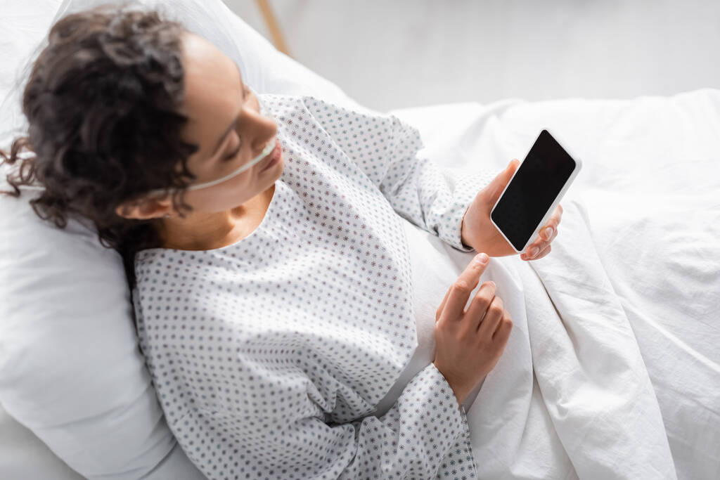 εναέρια άποψη των ασθενών αφροαμερικανή γυναίκα κρατώντας smartphone με λευκή οθόνη στην κλινική - Φωτογραφία, εικόνα
