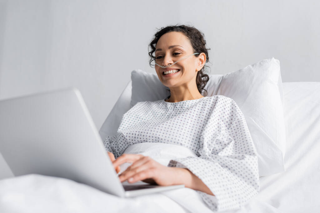 vrolijk Afrikaans amerikaans vrouw typen op laptop in ziekenhuis op wazig voorgrond - Foto, afbeelding