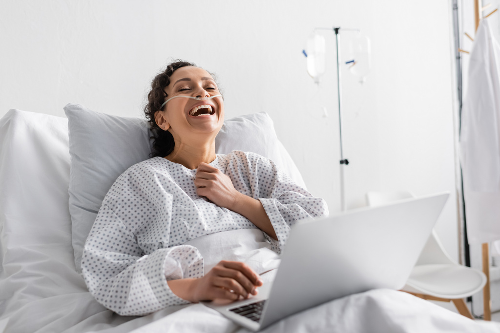 病院のラップトップでコメディ映画を見ながら笑うアフリカ系アメリカ人女性の興奮 - 写真・画像