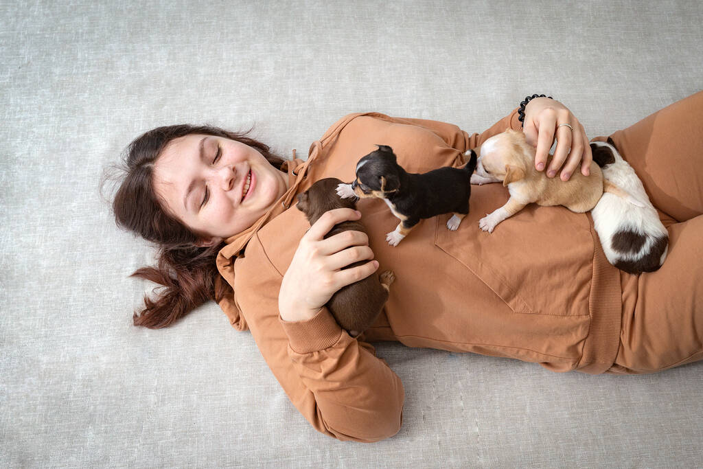 Een tienermeisje ligt op de grond met kleine puppy 's die op haar kruipen, het meisje lacht - Foto, afbeelding
