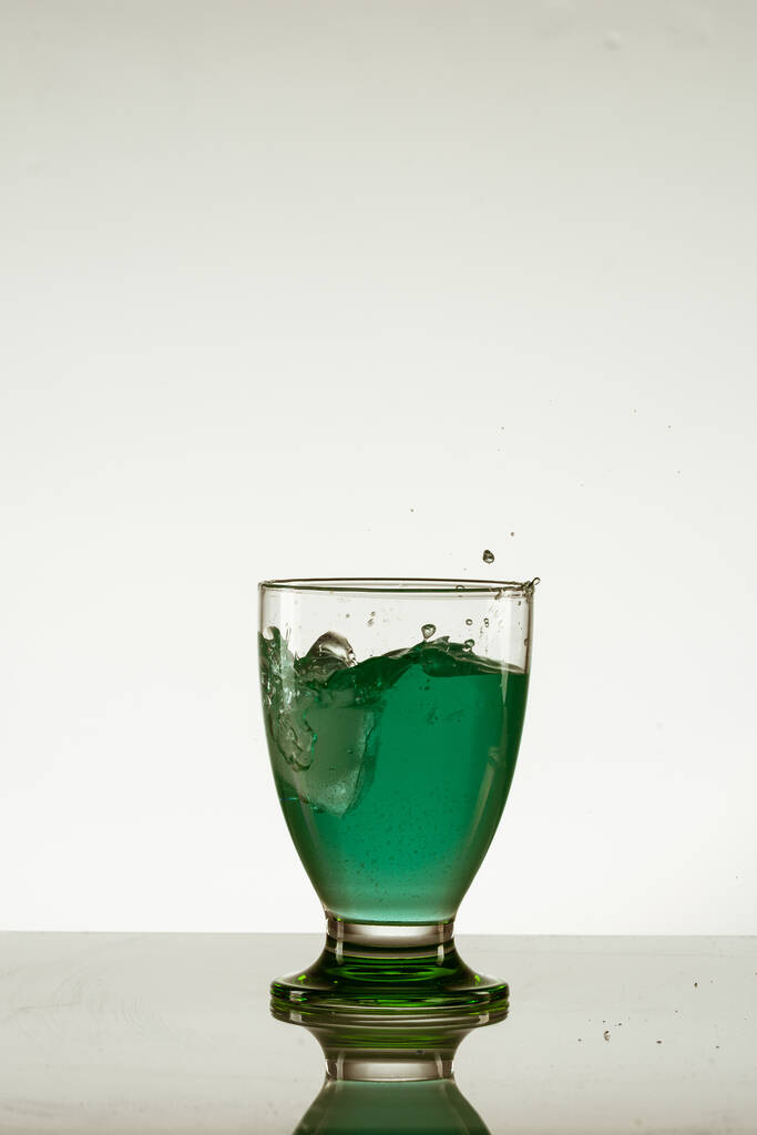 反射面に氷が隔離された緑の飲み物のガラスの垂直ショット - 写真・画像