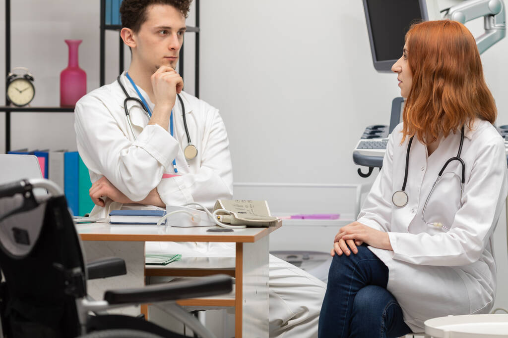 Um jovem médico fala com um estagiário ruivo sobre o próximo paciente. GP. Serviço de médicos - Foto, Imagem