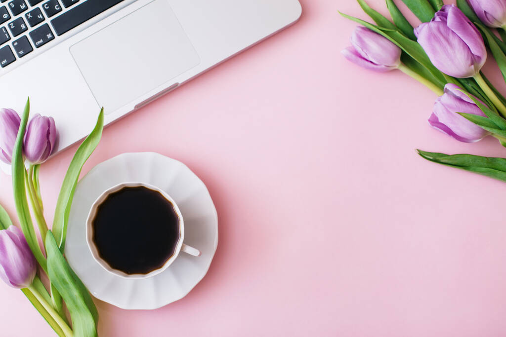 Spazio di lavoro con computer portatile, fiori di tulipano, tazza di caffè su sfondo rosa. Scrivania dell'ufficio. Layout piatto, vista dall'alto, spazio di copia per il testo. Concetto primavera - Foto, immagini