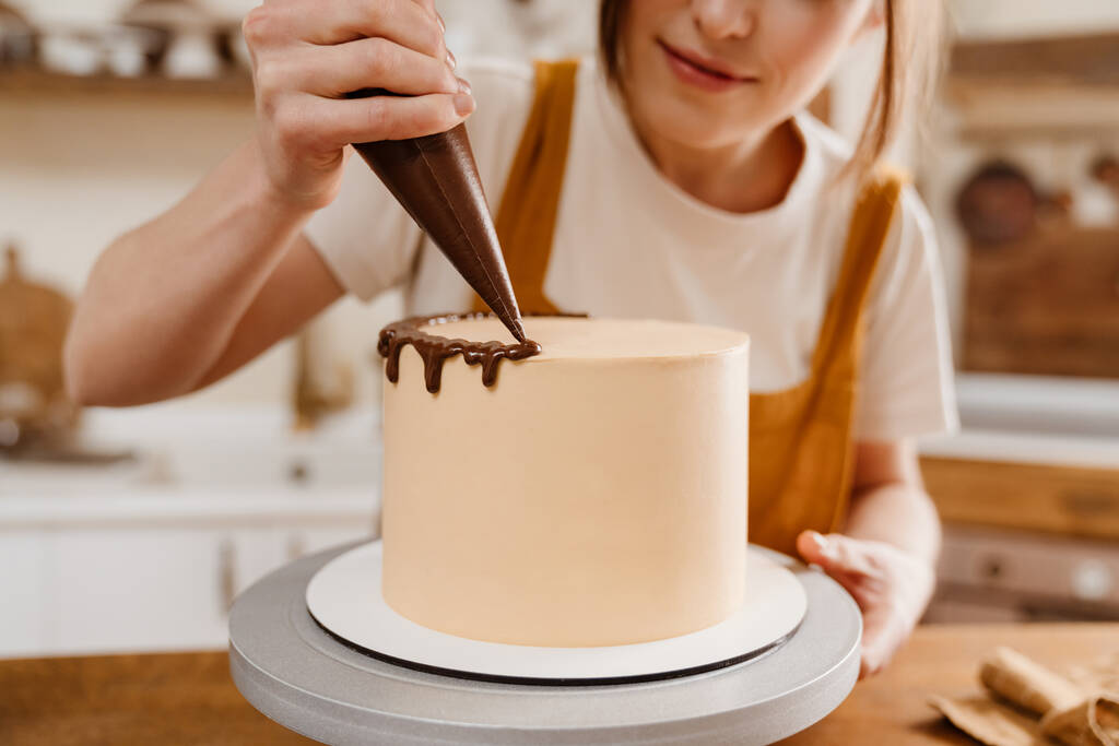 Belle femme chef pâtissier heureux faisant gâteau avec de la crème au chocolat à la cuisine confortable - Photo, image