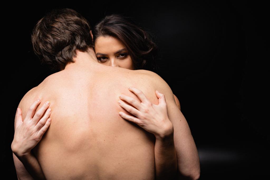 πίσω όψη του γυμνού άνδρα αγκαλιάζει μελαχρινή γυναίκα σε μαύρο - Φωτογραφία, εικόνα