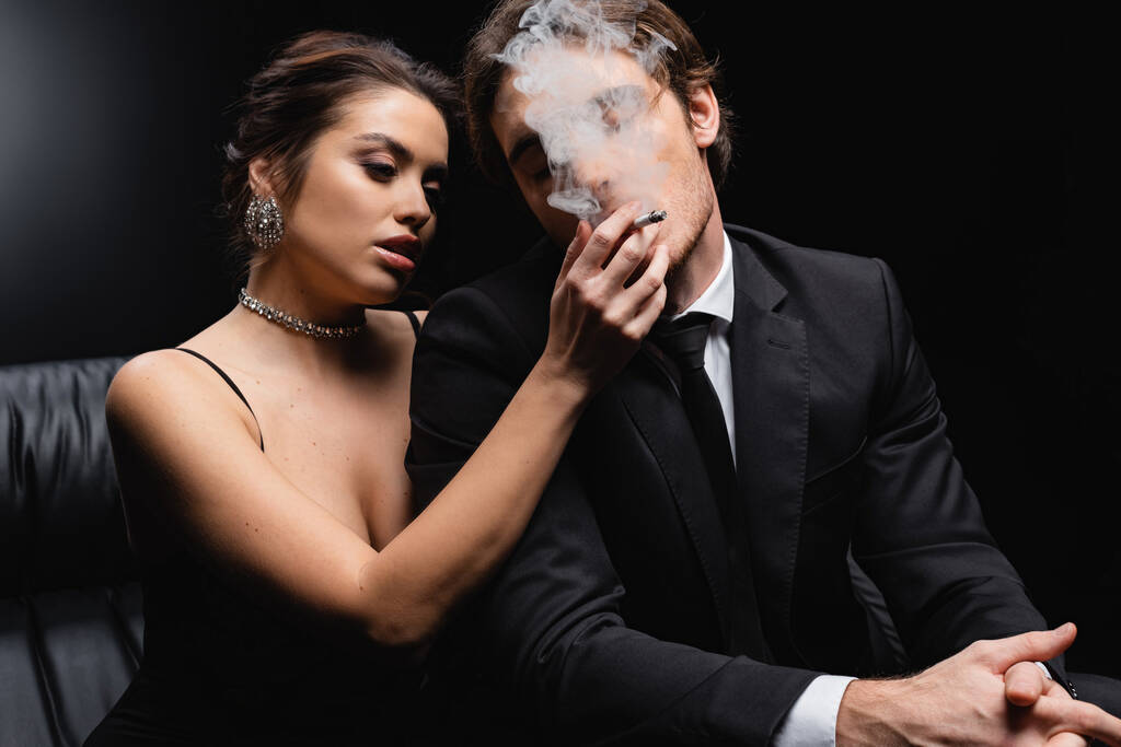 mulher sedutora em vestido deslizante segurando cigarro perto do homem de terno em preto  - Foto, Imagem