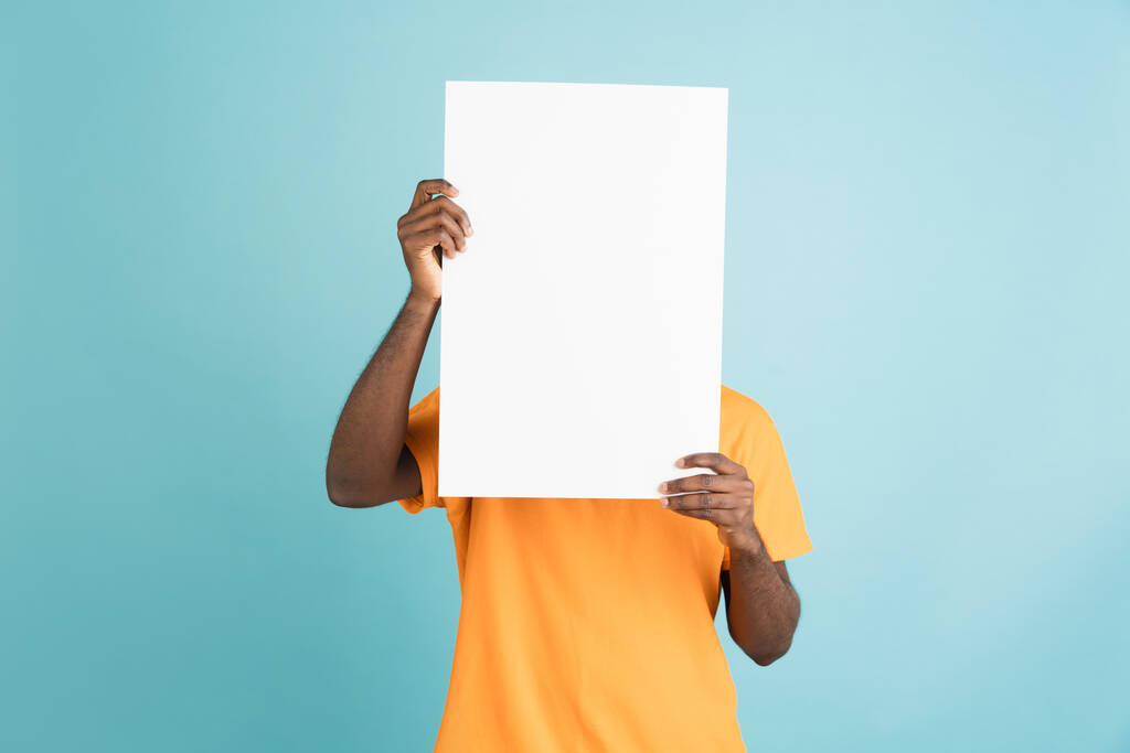 Молодой африканский человек с чистым листом бумаги изолирован на фоне синей студии. - Фото, изображение