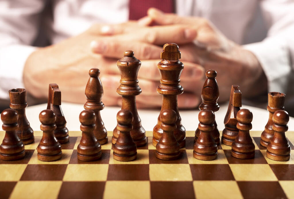 Schaakbord met schaakstukken en mannelijke handen op de achtergrond. Begrip bedrijfsstrategie - Foto, afbeelding