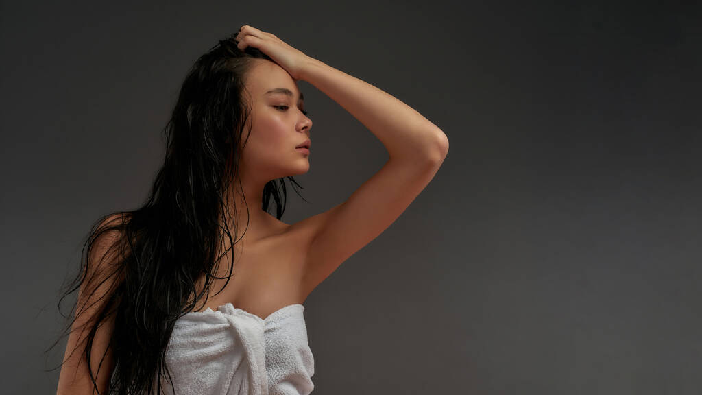 Joven hermosa asiática mitad mujer desnuda en toalla de baño con parches cosméticos para los ojos de pie media cara - Foto, Imagen