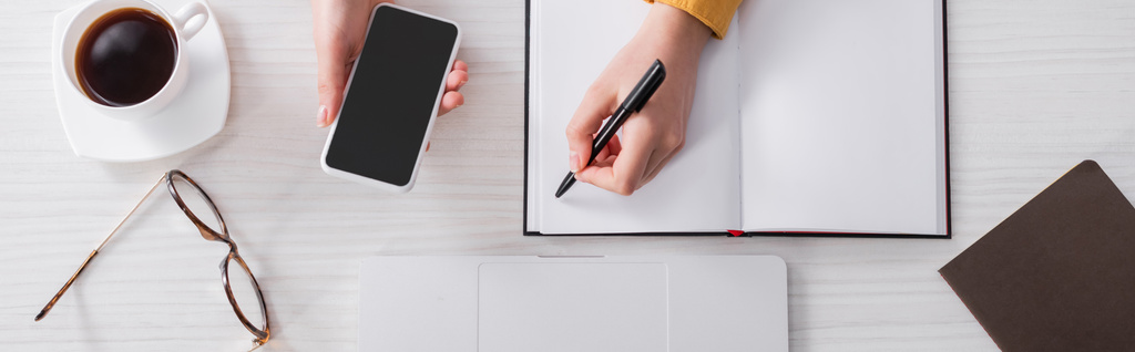 vista recortada de freelancer segurando caneta e smartphone perto de notebook vazio, banner - Foto, Imagem