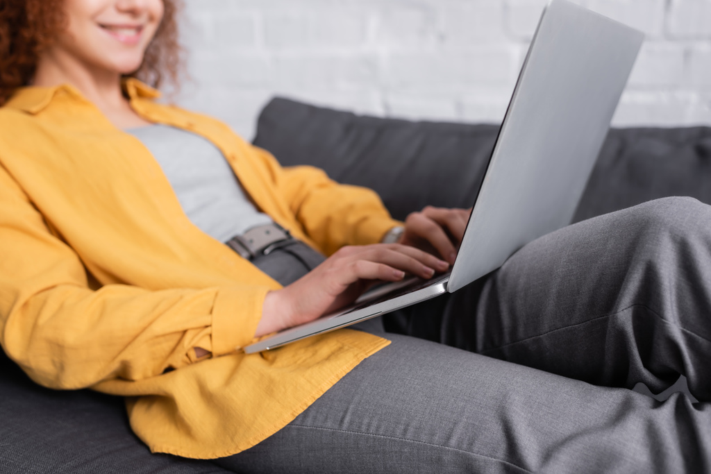 corte vista de sorrindo freelancer digitando no laptop no sofá, fundo borrado - Foto, Imagem