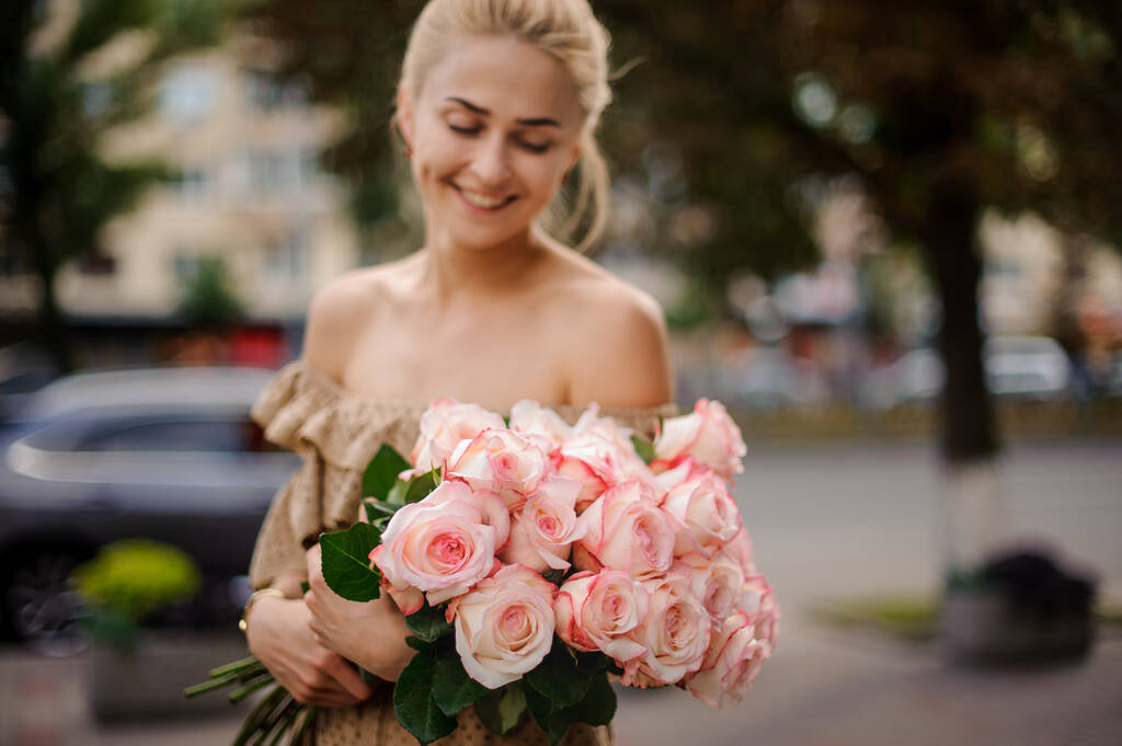 Magnifique bouquet de belles roses roses entre les mains d'une jeune femme souriante - Photo, image