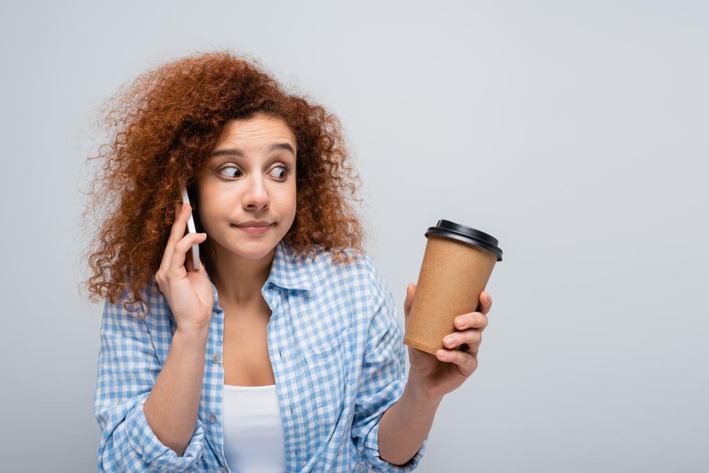 заплутана жінка дивиться на паперову чашку, розмовляючи на мобільному телефоні ізольовано на сірому
 - Фото, зображення