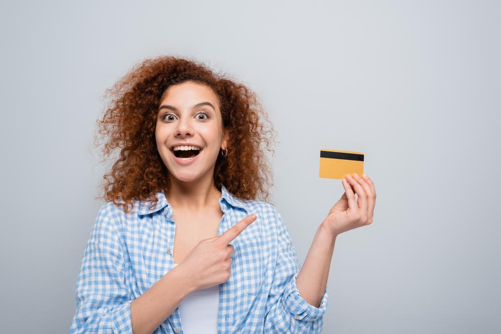 вражена жінка в простій сорочці, вказуючи на кредитну картку ізольовано на сірому
 - Фото, зображення