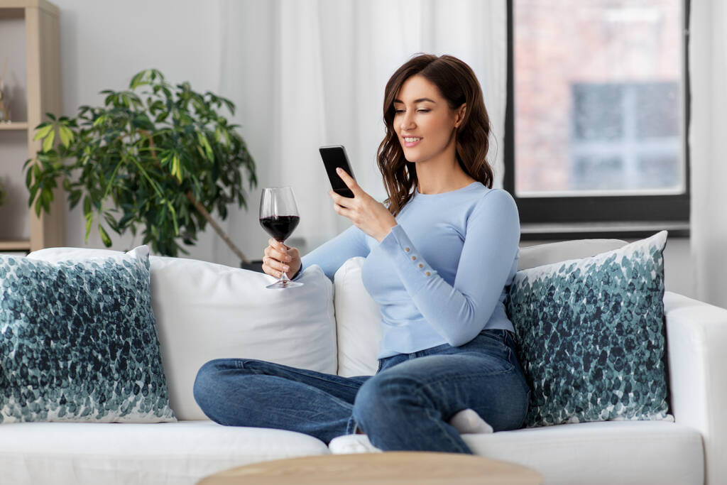 donna con smartphone bere vino rosso a casa - Foto, immagini