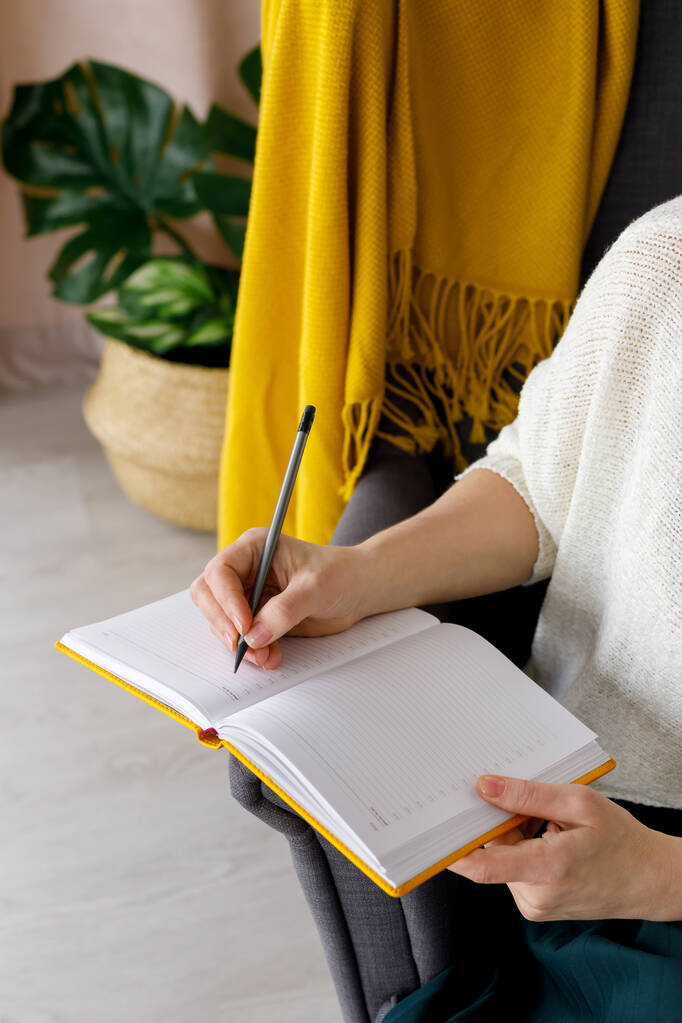 blogger mujer hace notas en un cuaderno amarillo. Programación de tareas para el día. Llevando un diario. Horario posterior - Foto, imagen