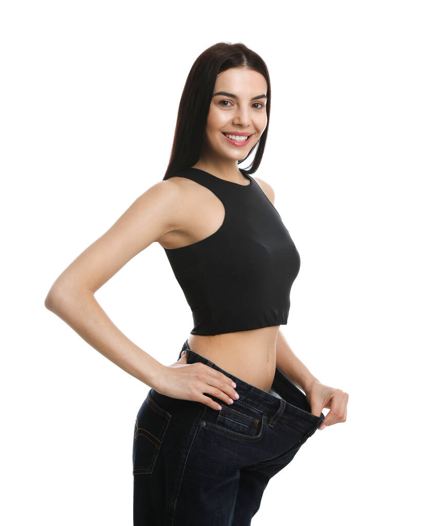 Mujer joven feliz con pantalones vaqueros grandes después de la pérdida de peso sobre fondo blanco - Foto, Imagen