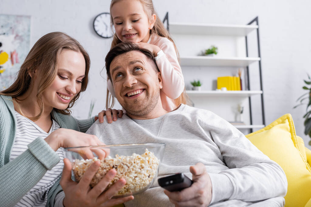 Pozytywne dziecko patrzące na rodziców z popcornem i pilotem  - Zdjęcie, obraz