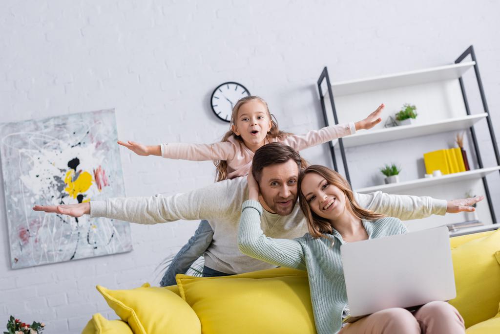 Man and daughter having fun near smiling wife using laptop at home  - Photo, Image