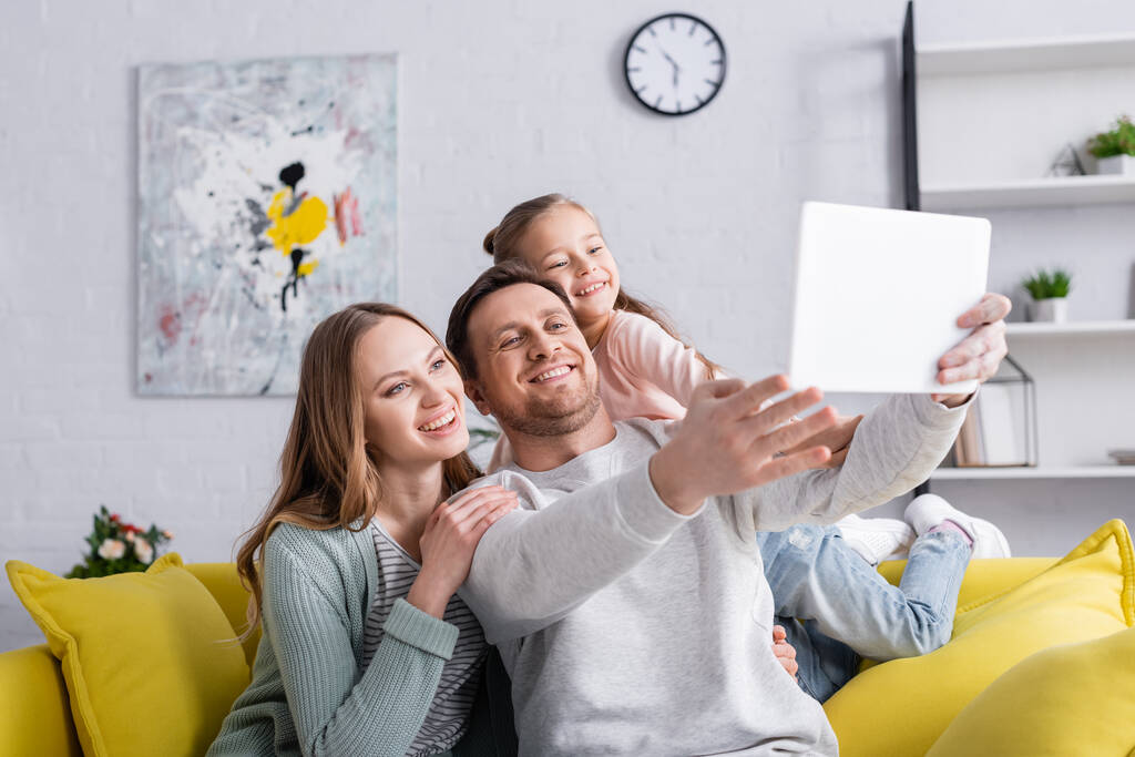 Familia sonriente usando tableta digital en primer plano borroso en casa  - Foto, Imagen