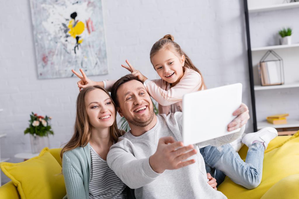 Gülümseyen çocuk dijital tablette selfie çeken ebeveynlerin yanında parmaklarıyla tavşan kulakları gösteriyor.  - Fotoğraf, Görsel