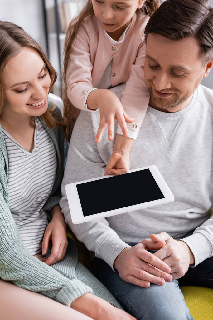Tablet cyfrowy z pustym ekranem w ręku dziecka w pobliżu uśmiechniętych rodziców w domu  - Zdjęcie, obraz