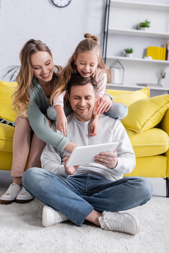 Mann mit digitalem Tablet auf dem Boden neben Familie auf Couch  - Foto, Bild