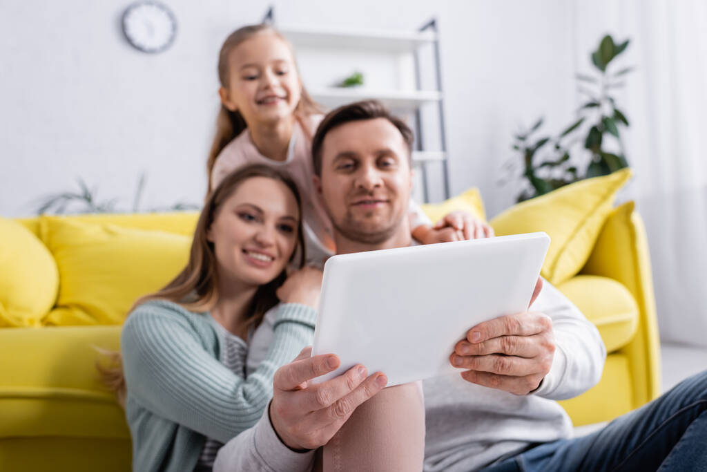 Digital tablet in hands of man on blurred background near family  - Photo, Image
