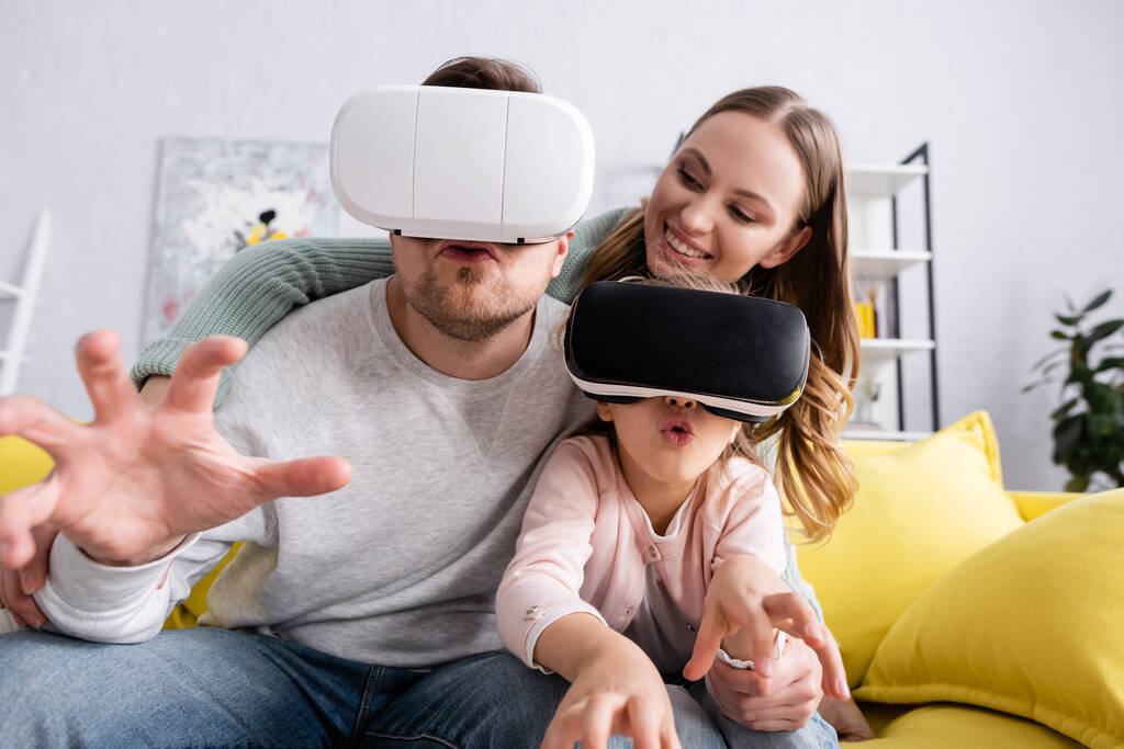 Excited child and father using vr headsets near smiling mother  - Photo, Image