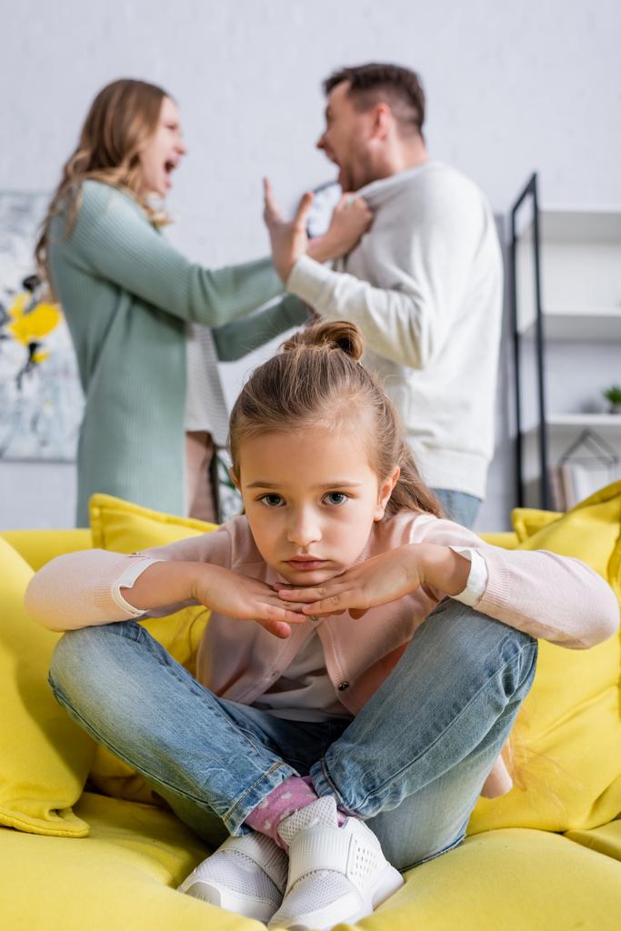 Сумна дитина сидить на дивані біля батьків, що конфліктують
  - Фото, зображення