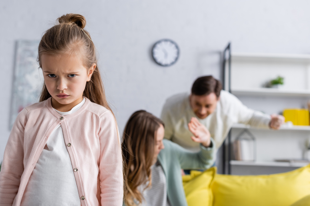 Niezadowolony dzieciak patrząc w aparat podczas kłótni rodziców  - Zdjęcie, obraz