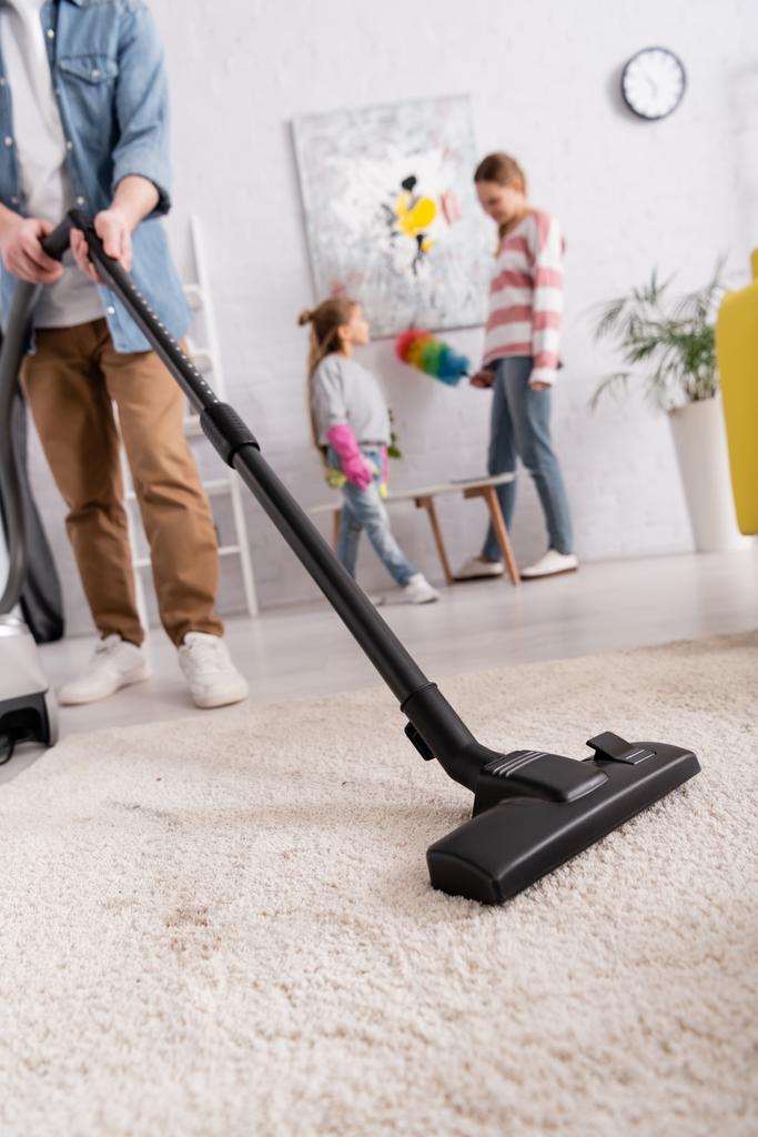 Man cleaning carpet near family on blurred background at home  - Photo, Image