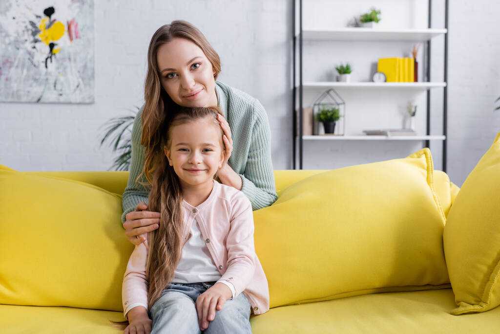 Boldog lány néz kamera közelében szülő sárga kanapén  - Fotó, kép