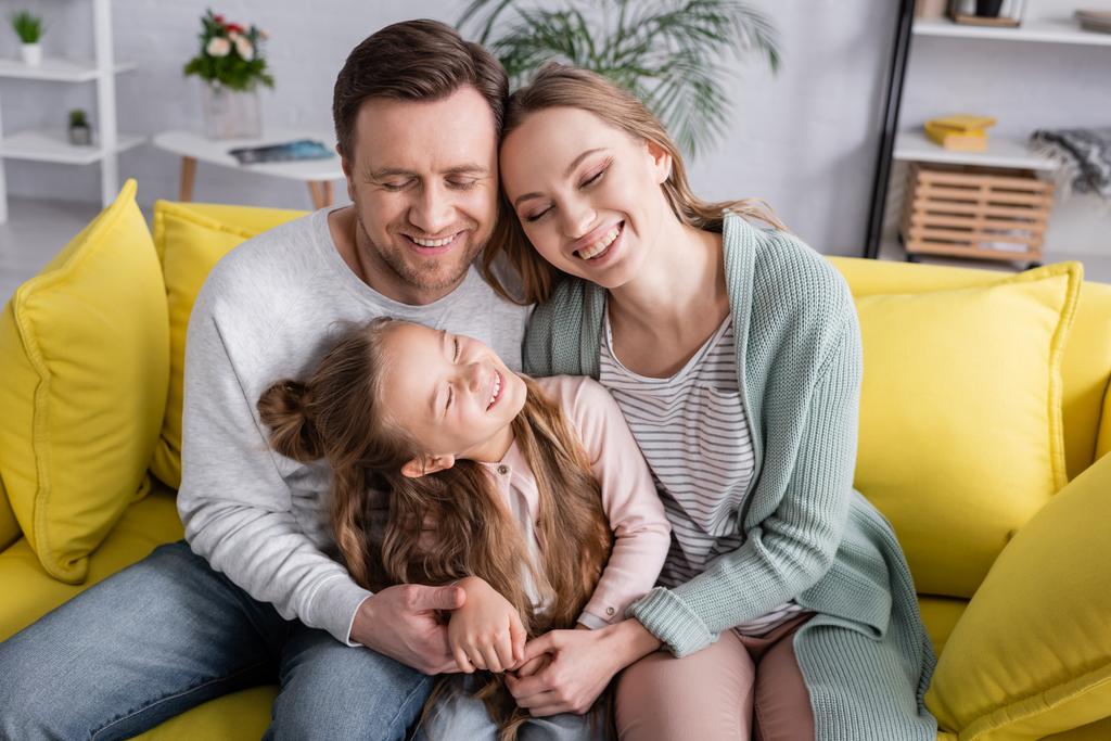 Szczęśliwa rodzina z zamkniętymi oczami przytulająca się na kanapie  - Zdjęcie, obraz