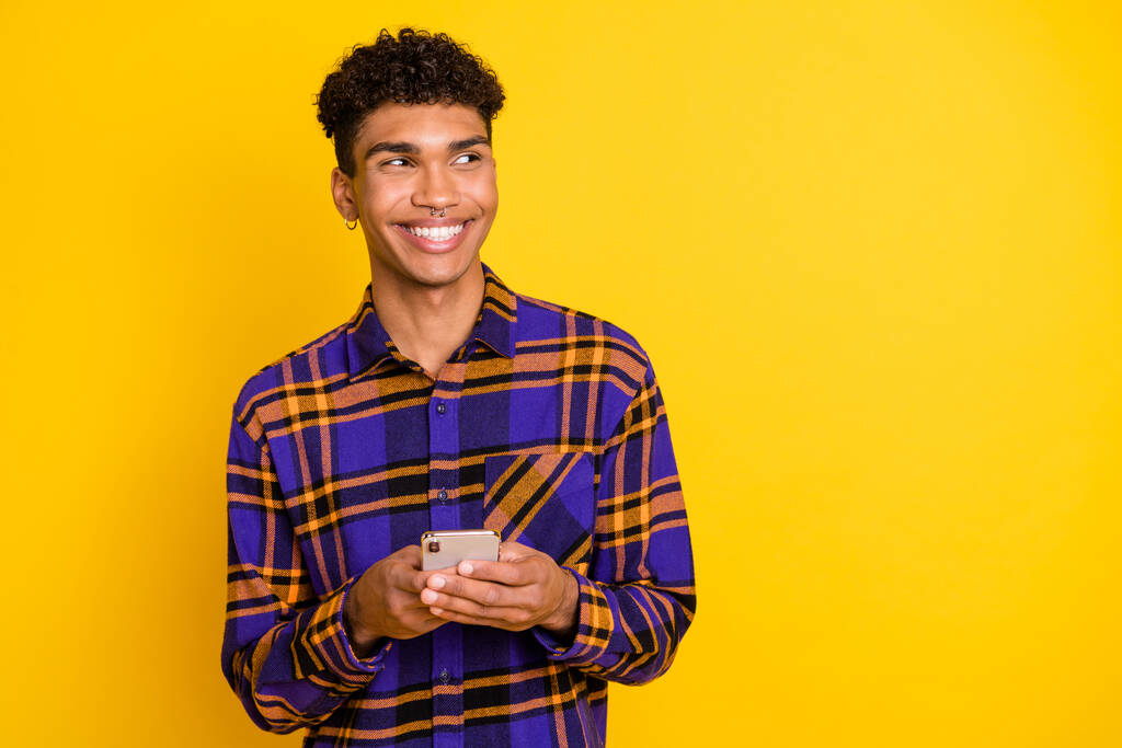 Zdjęcie portret człowieka przeglądającego internet telefon komórkowy patrząc puste miejsce w kratkę strój izolowany na żywy żółty kolor tła - Zdjęcie, obraz