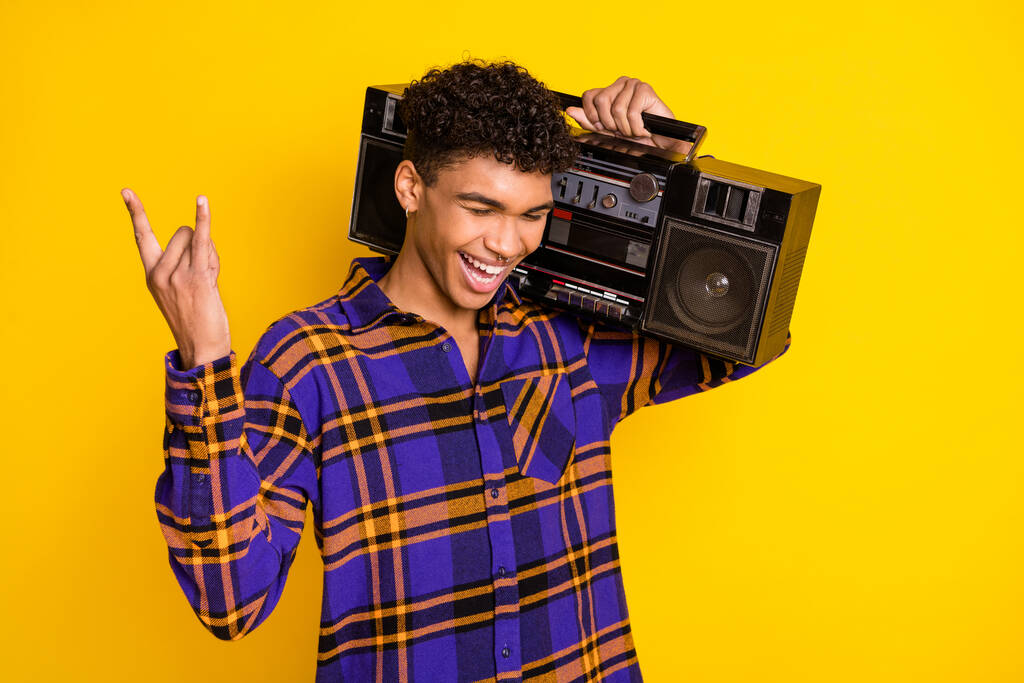 Photo portrait of handsome guy smiling keeping boom box showing heavy metal isolated on vivid yellow color background - Photo, Image