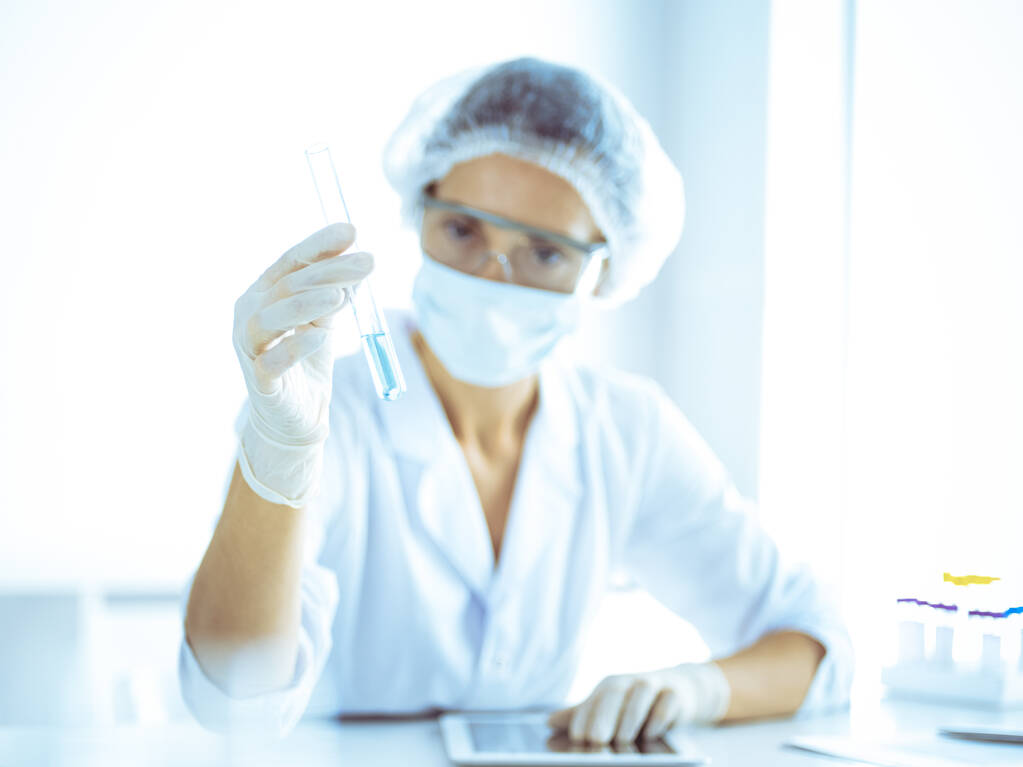Professionelle Wissenschaftlerin mit Schutzbrille, die Röhre mit Reagenzien im Labor untersucht. Konzepte von Medizin und Forschung - Foto, Bild